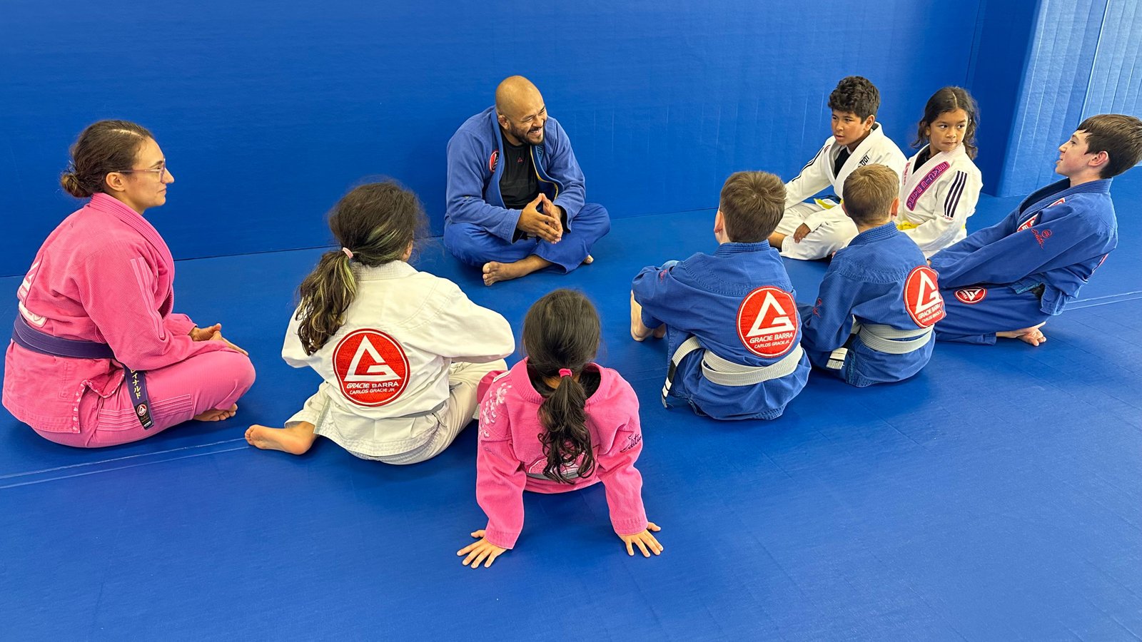 Professor Thiago Reinaldo smiling while seated with young students at Gracie Barra Stafford
